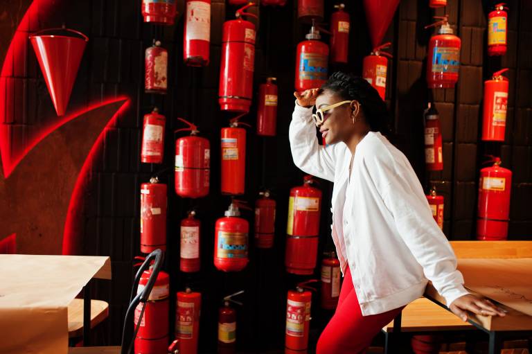 African woman posed against wall with old extinguisher.