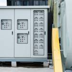 The electrical room of a commercial building contains multiple smart meters, a main power breaker, and various meter stacks and cabinets.