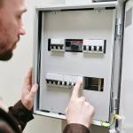 Young man in workwear standing in front of voltage panel